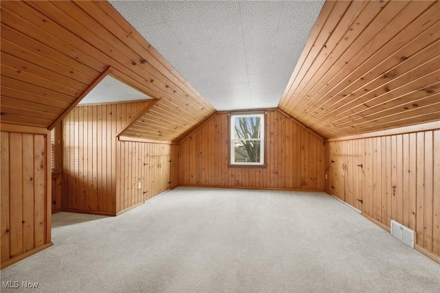 additional living space featuring visible vents, carpet floors, lofted ceiling, and wood walls