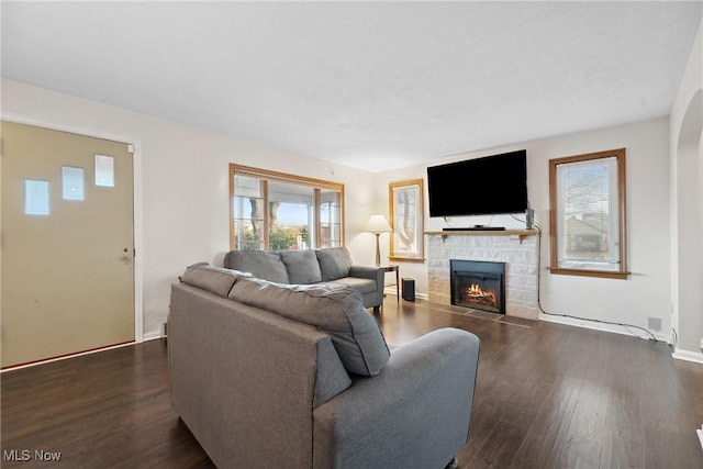 living area with dark wood-style floors, a stone fireplace, and baseboards