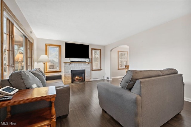 living area featuring a stone fireplace, dark wood-style floors, baseboards, and arched walkways