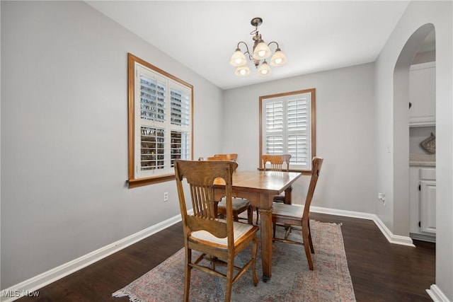 dining space with baseboards, arched walkways, an inviting chandelier, and wood finished floors