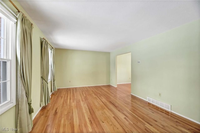 empty room featuring visible vents, a healthy amount of sunlight, and light wood finished floors