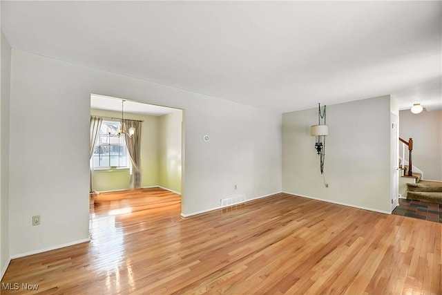 unfurnished room featuring a notable chandelier, stairway, visible vents, and wood finished floors