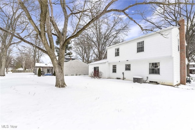 snow covered property with central air condition unit and a chimney