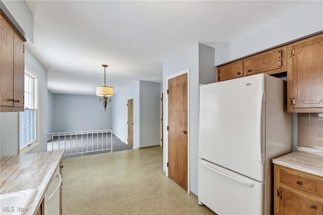 kitchen featuring brown cabinets, decorative light fixtures, a sink, white appliances, and light countertops