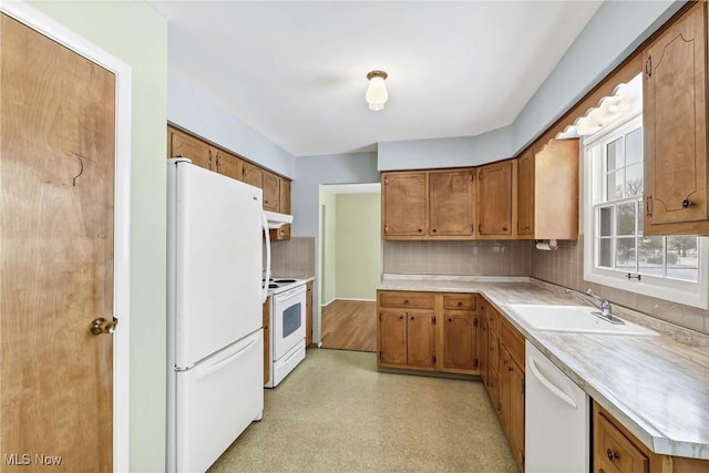 kitchen featuring brown cabinetry, white appliances, light countertops, and a sink