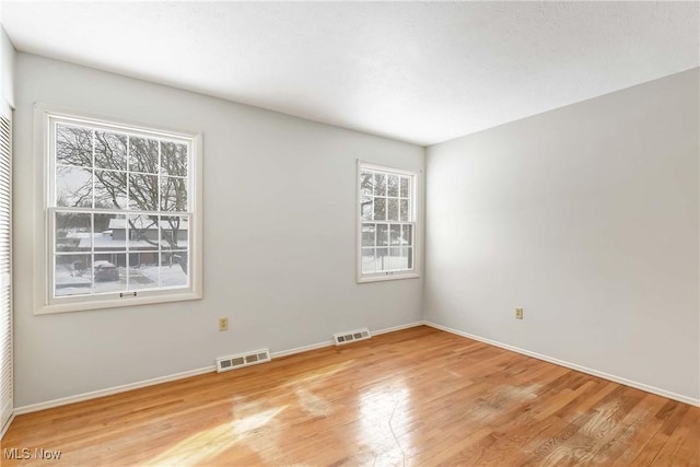 empty room featuring wood finished floors, visible vents, and baseboards