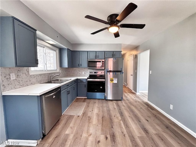 kitchen with a sink, backsplash, appliances with stainless steel finishes, light countertops, and baseboards