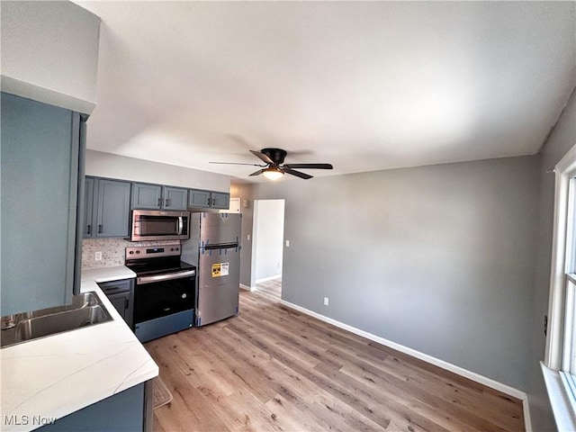 kitchen with appliances with stainless steel finishes, light wood finished floors, decorative backsplash, baseboards, and light countertops