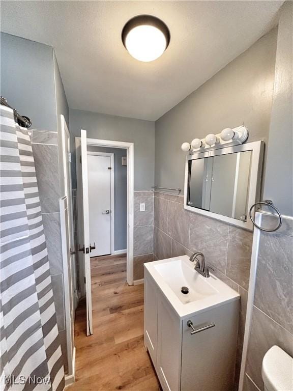 full bathroom with vanity, a shower with curtain, wood finished floors, tile walls, and toilet