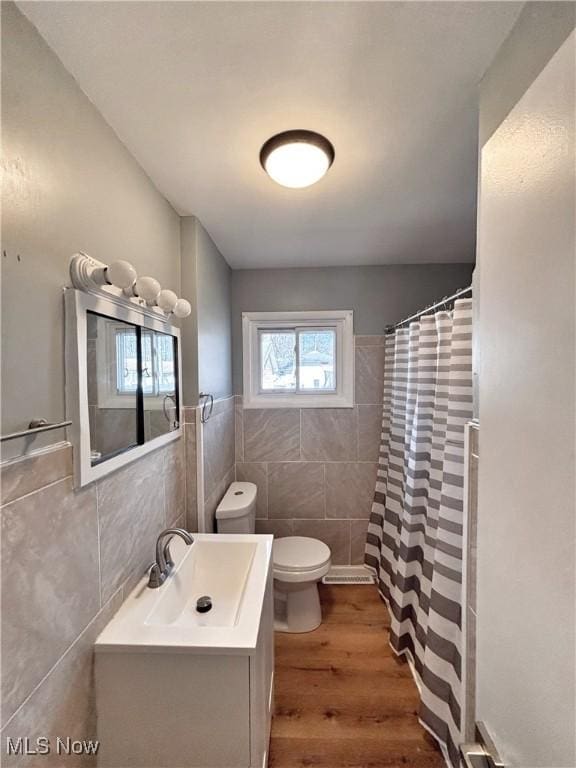 bathroom featuring curtained shower, tile walls, toilet, wood finished floors, and vanity