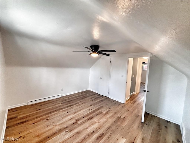 additional living space with a baseboard heating unit, lofted ceiling, a textured ceiling, and wood finished floors