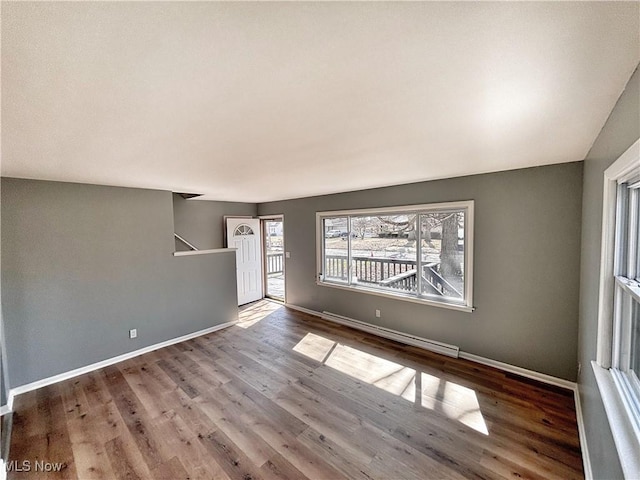 unfurnished room featuring baseboards, baseboard heating, and wood finished floors