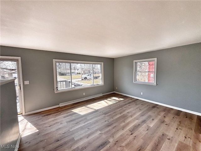 unfurnished room featuring a baseboard heating unit, plenty of natural light, and wood finished floors