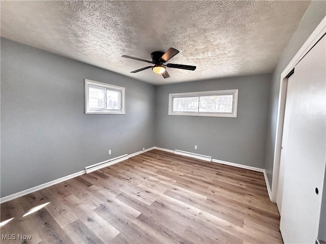 unfurnished bedroom featuring baseboard heating, multiple windows, a baseboard radiator, and wood finished floors