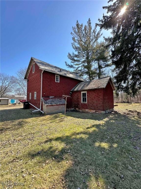 back of house with brick siding and a lawn