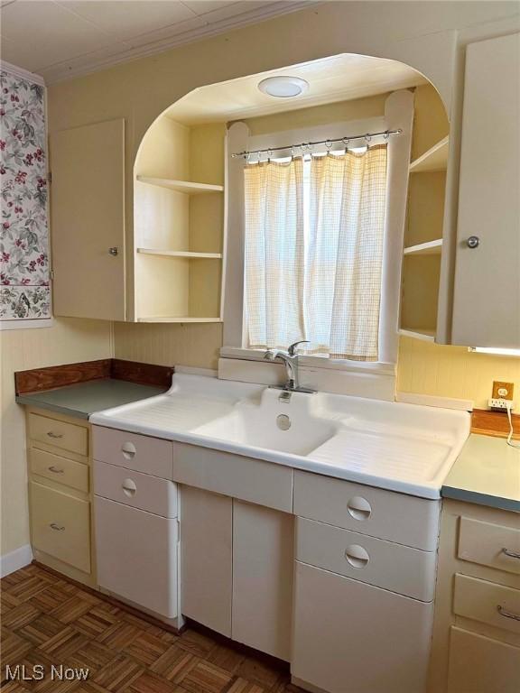 kitchen featuring open shelves, crown molding, light countertops, arched walkways, and a sink