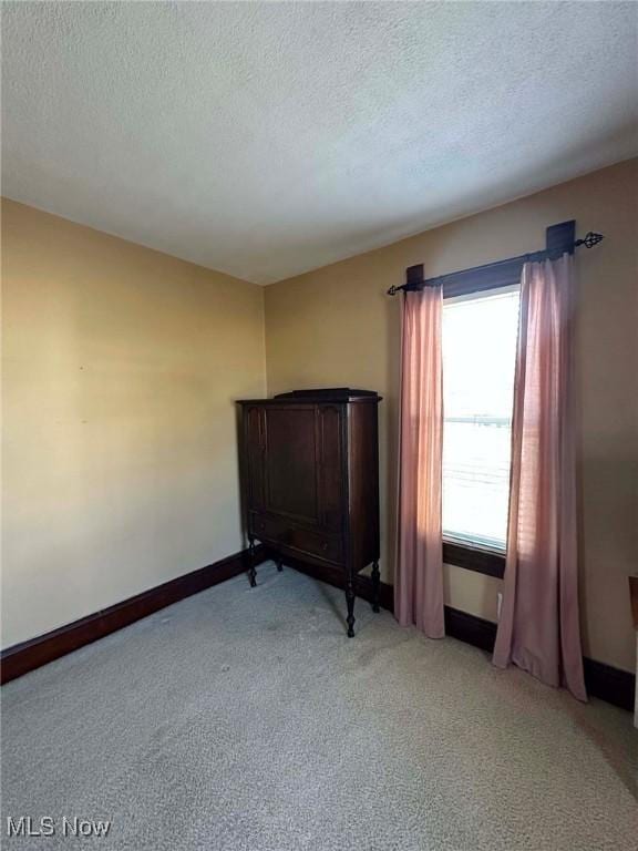 unfurnished room with light colored carpet, baseboards, and a textured ceiling