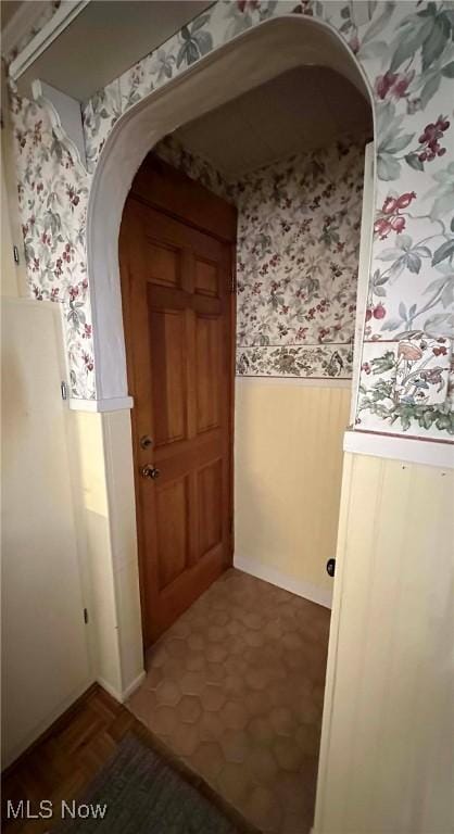 hallway featuring arched walkways, wainscoting, and wallpapered walls