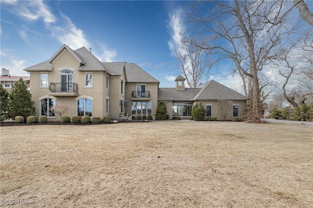 french country inspired facade featuring stucco siding, a balcony, and a front lawn