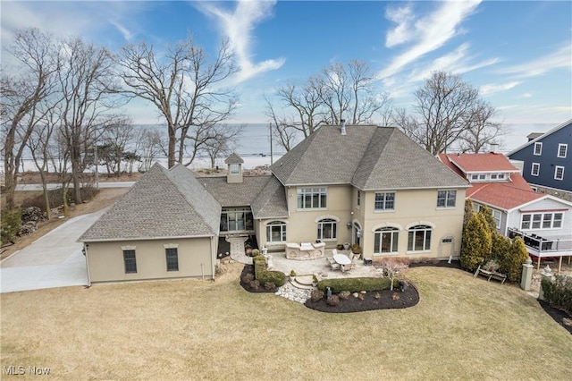 rear view of property with stucco siding, a patio, a lawn, and a shingled roof