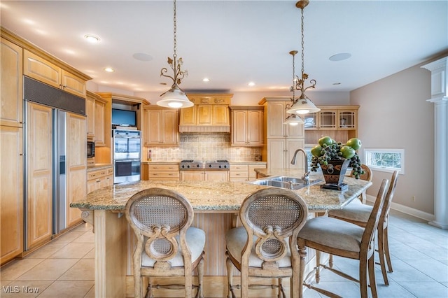 kitchen featuring backsplash, premium range hood, light tile patterned floors, appliances with stainless steel finishes, and a sink