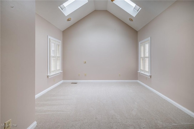 empty room featuring baseboards, high vaulted ceiling, light carpet, and a skylight