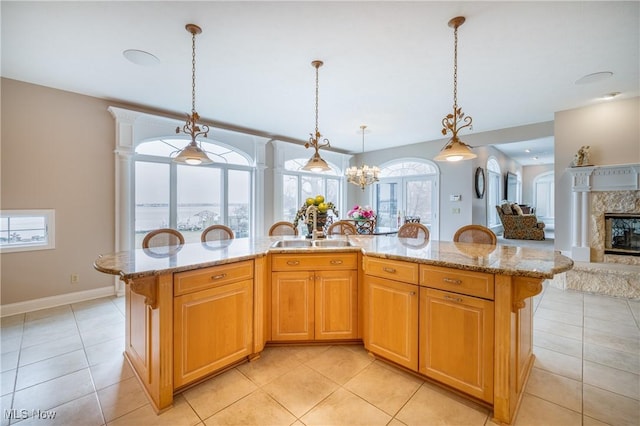 kitchen featuring open floor plan, light stone counters, light tile patterned floors, a fireplace, and a sink