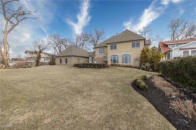 back of property with a lawn and stucco siding