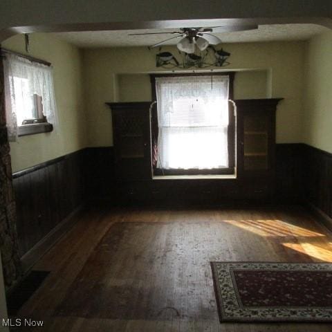 spare room featuring a wainscoted wall, arched walkways, wood finished floors, and a ceiling fan