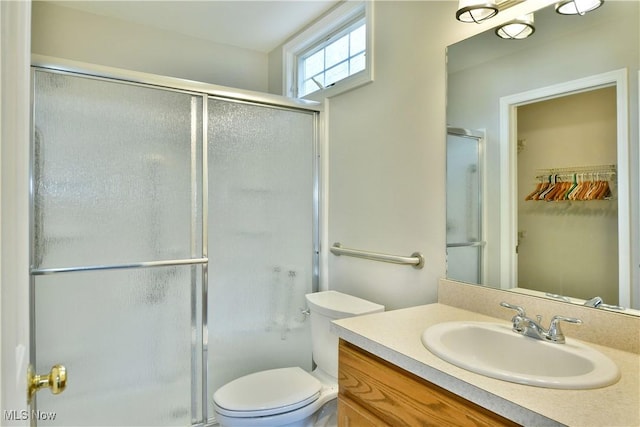 full bath featuring vanity, a shower stall, a walk in closet, and toilet