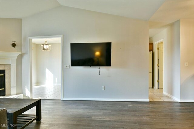 unfurnished living room with a tiled fireplace, vaulted ceiling, baseboards, and wood finished floors