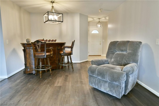 sitting room with a dry bar, wood finished floors, baseboards, and a chandelier