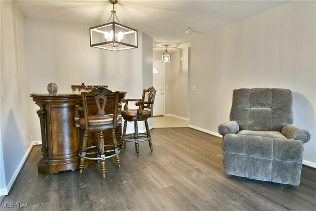 sitting room featuring a bar, wood finished floors, baseboards, and a chandelier