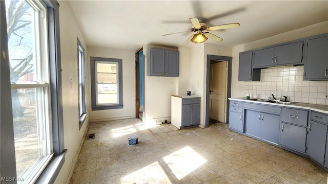 kitchen featuring a ceiling fan, gray cabinetry, a sink, light countertops, and tasteful backsplash