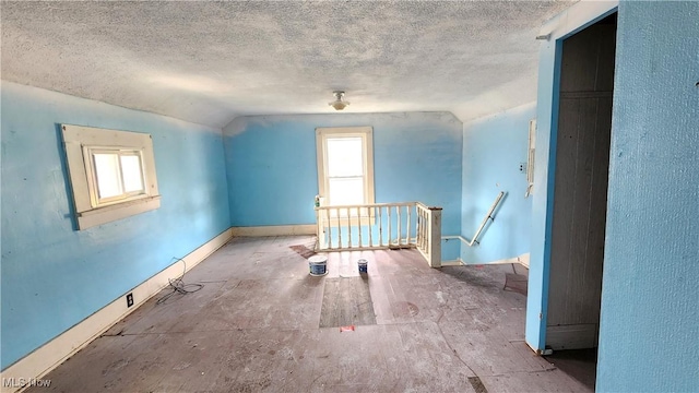 additional living space with baseboards, lofted ceiling, a textured ceiling, and a healthy amount of sunlight