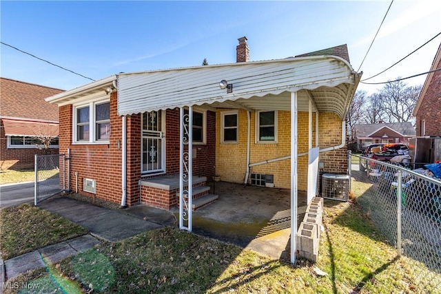 view of front facade featuring central air condition unit, a chimney, fence, an attached carport, and brick siding