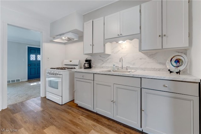 kitchen featuring visible vents, a sink, decorative backsplash, white gas range oven, and under cabinet range hood