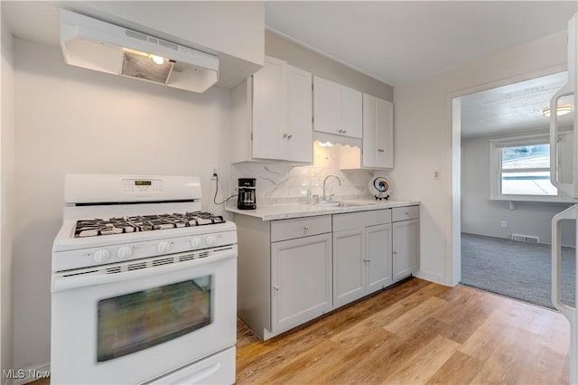 kitchen with visible vents, white range with gas cooktop, a sink, under cabinet range hood, and backsplash