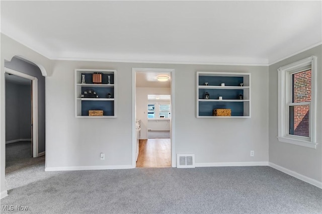 carpeted empty room with built in features, arched walkways, visible vents, and baseboards