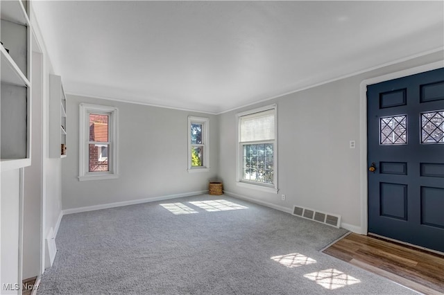 carpeted entrance foyer featuring visible vents, baseboards, and ornamental molding