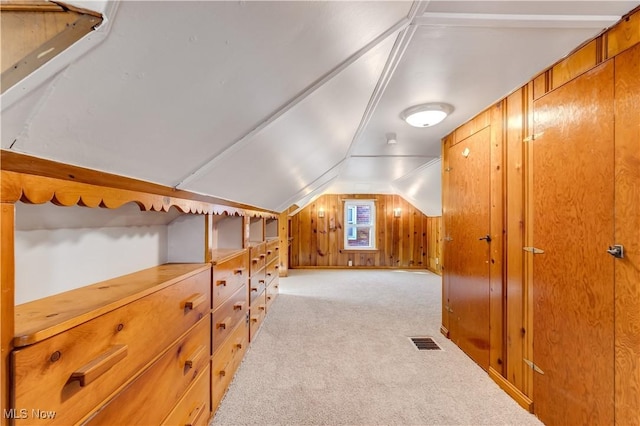 additional living space with lofted ceiling, visible vents, carpet floors, and wood walls