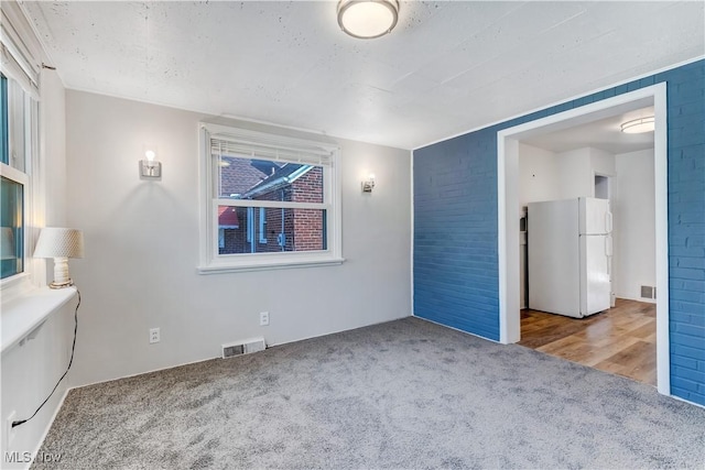 unfurnished bedroom featuring visible vents, freestanding refrigerator, and carpet floors