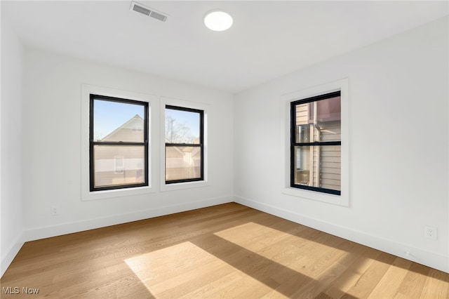 empty room with wood finished floors, visible vents, and baseboards