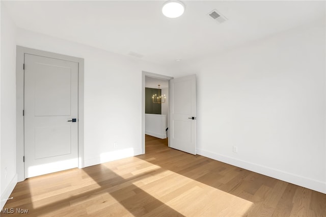 unfurnished room with visible vents, baseboards, an inviting chandelier, and wood finished floors