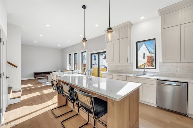 kitchen with light wood-type flooring, a sink, decorative backsplash, stainless steel dishwasher, and open floor plan