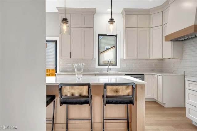 kitchen featuring a sink, custom exhaust hood, a breakfast bar, and light countertops