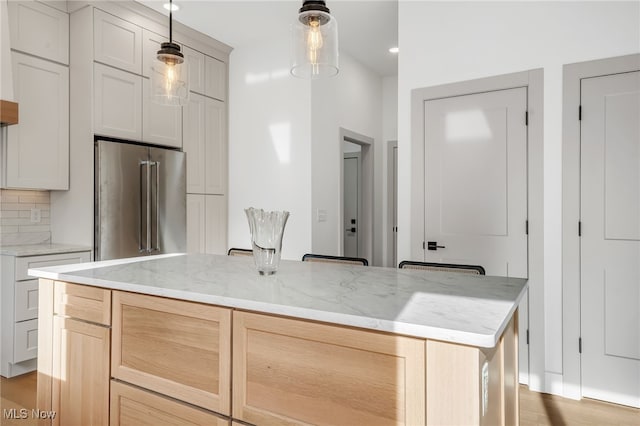 kitchen featuring light stone countertops, high end refrigerator, light wood-type flooring, backsplash, and a center island