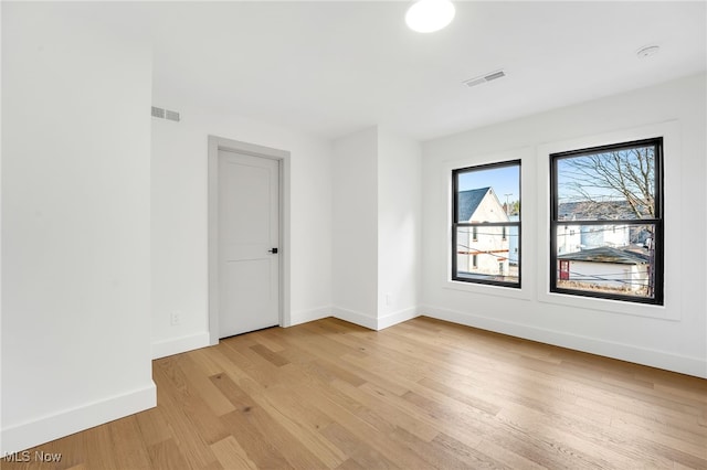 empty room with light wood-type flooring, visible vents, and baseboards