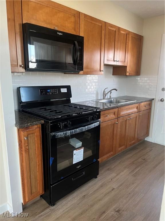 kitchen featuring a sink, dark countertops, light wood-style floors, and black appliances