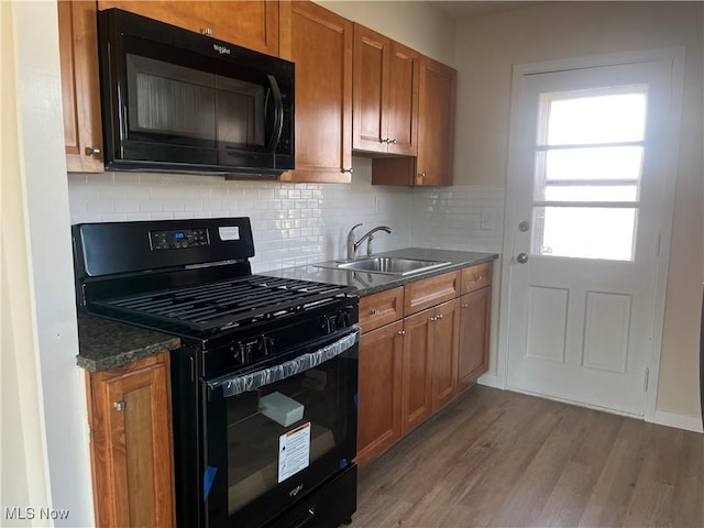 kitchen featuring tasteful backsplash, brown cabinets, wood finished floors, black appliances, and a sink